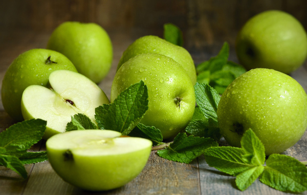 Зеленые яблоки в каплях воды на столе с мятой