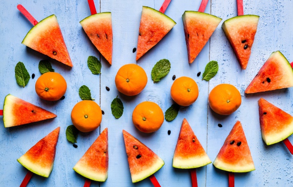 Кусочки арбуза на палочках на столе с мандаринами