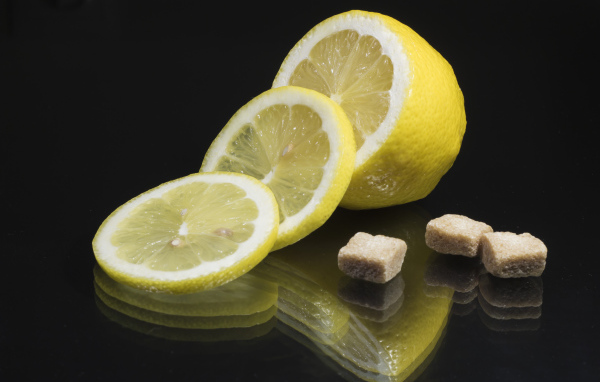 Нарезанный лимон с кусочками коричневого сахара на черном фоне