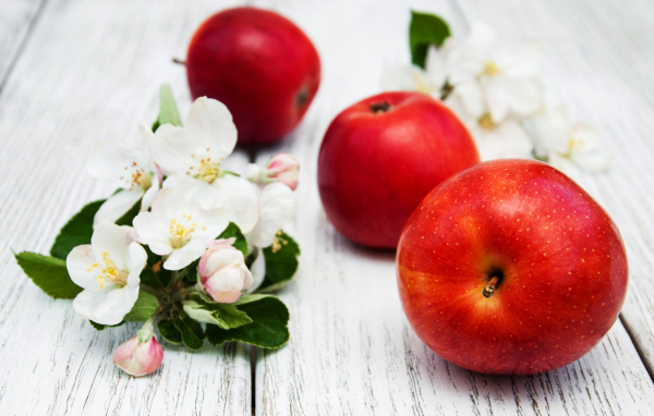 Три красных яблока с цветами на деревянной поверхности