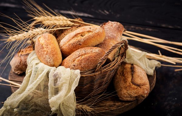 Свежая выпечка в корзине на столе с колосьями пшеницы