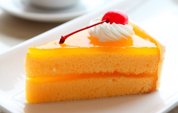 Кусок апельсинового торта с вишенкой на белой тарелке