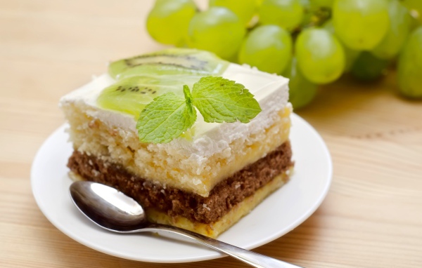 Кусок торта с киви и мятой на столе с виноградом
