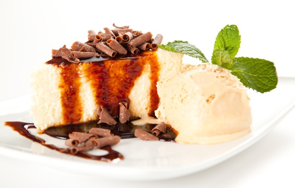 Кусок чизкейка с шоколадом и шариком мороженого на белой тарелке 