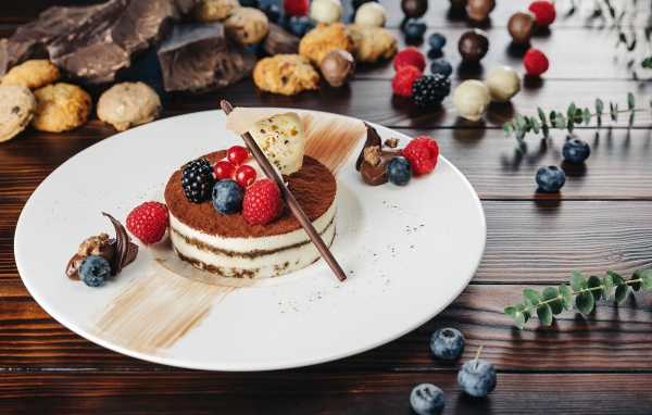 Пирожное с ягодами и шоколадом на белой тарелке 