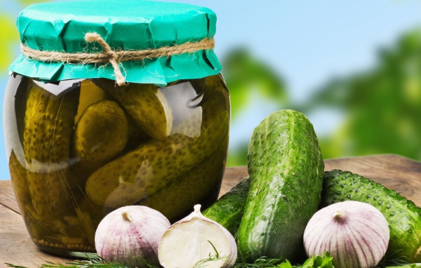 Консервированные огурцы в банке на столе со свежими огурцами и чесноком