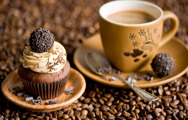 Кекс с кремом и чашкой кофе стоят на кофейных зернах 