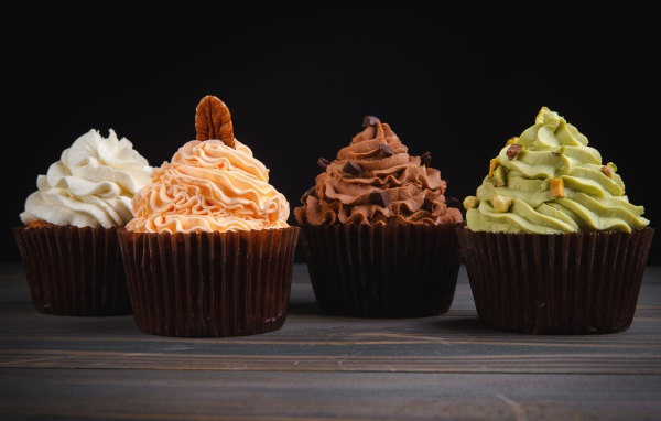Четыре аппетитных капкейка с кремом на черном фоне