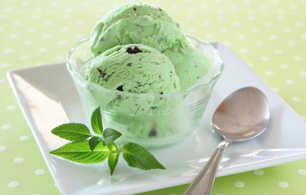 Зеленые шарики мороженого с шоколадом и мятой на тарелке с ложкой