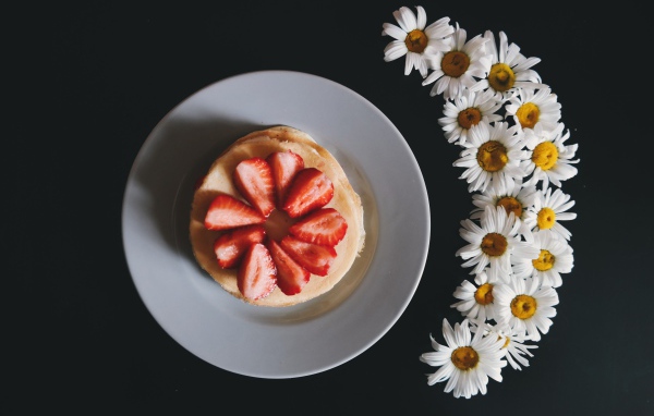 Оладьи с клубникой на тарелке на сером фоне с ромашками