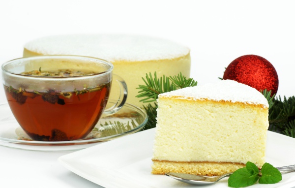 Кусок чизкейка на белой тарелке с чашкой чая на белом фоне