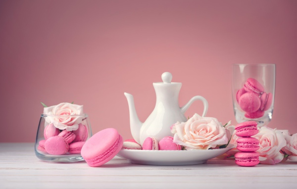 Розовый десерт макарун на столе с белый чайником и цветами розы