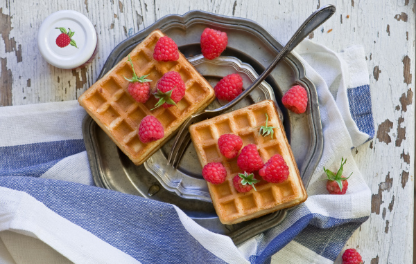 Сладкие вафли с ягодами малины на столе 