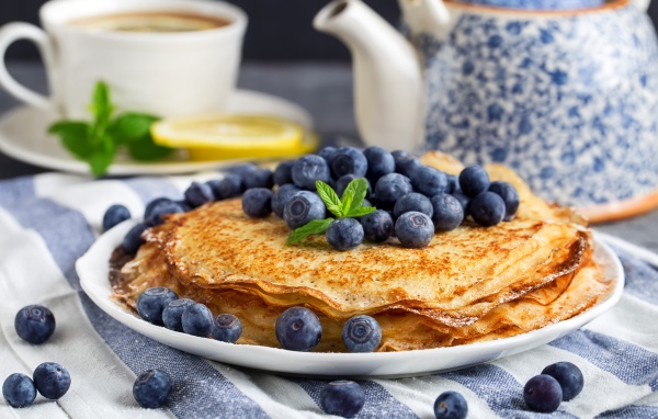 Тонкие блины с ягодами черники на столе с чаем