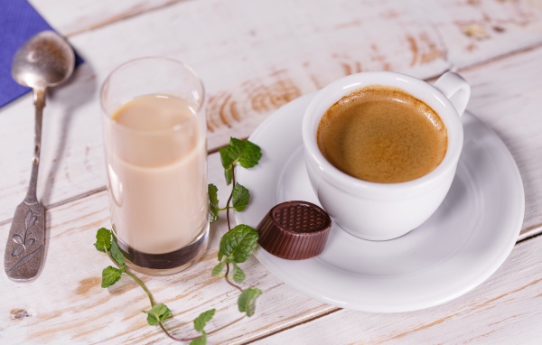 Чашка кофе с шоколадной конфетой и стаканом молока на столе