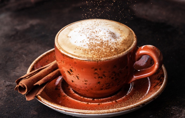 Чашка кофе с пенкой на блюдце с корицей