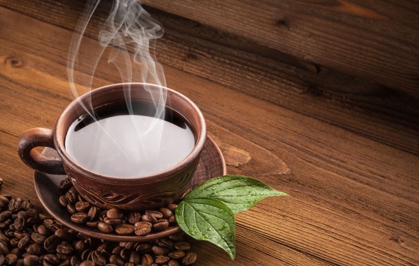 Чашка горячего кофе с зернами на деревянном столе