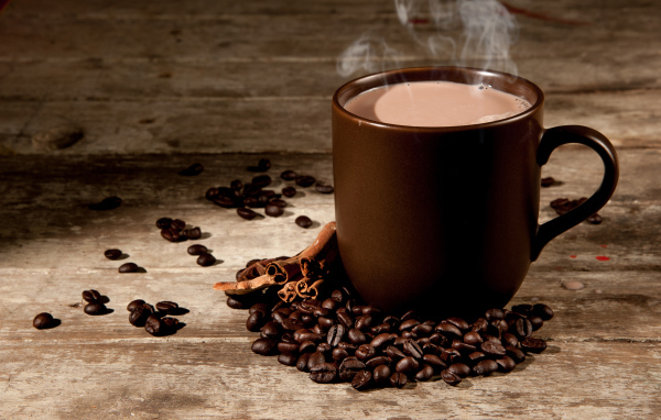 Чашка горячего кофе с молоком на столе с корицей и кофейными зернами