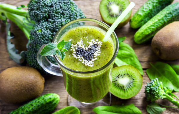 Стакан зеленого смузи на столе с киви, огурцами и брокколи