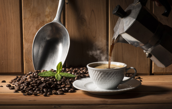 Горячий кофе наливают в чашку на столе с кофейными зернами