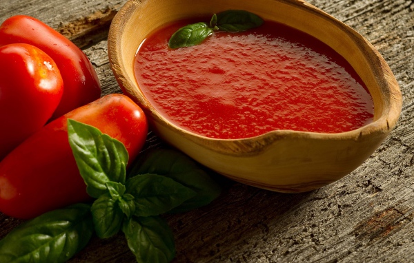 Томатный сок в деревянной посуде на столе с помидорами и базиликом