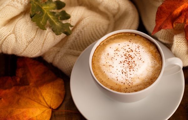 Белая чашка с вкусным кофе на столе с желтыми листьями