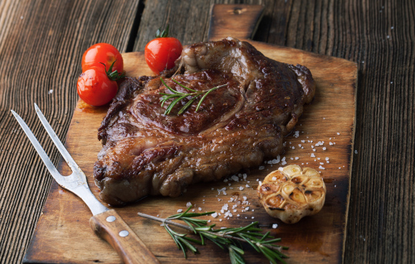 Кусок жареного мяса на разделочной доске с помидорами и чесноком