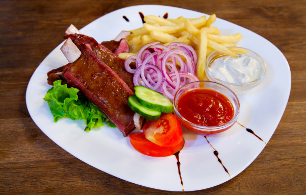 Мясо с овощами и картофелем фри на большой белой тарелке с соусом