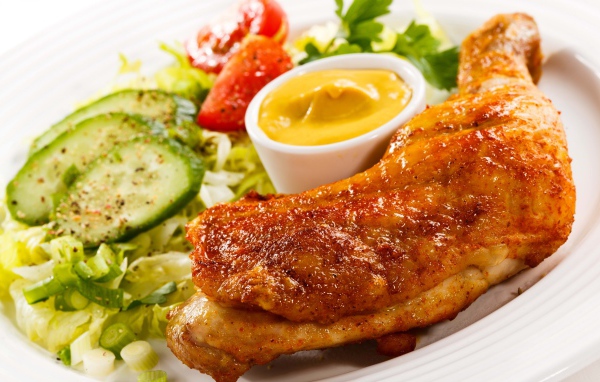 Жареная куриная ножка с овощами и соусом на тарелке