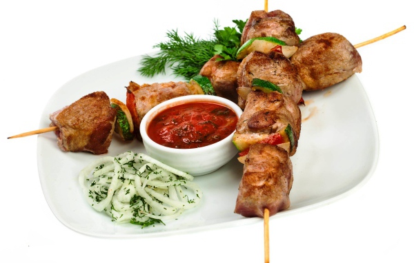 Шашлык на белой тарелке с соусом, зеленью и луком