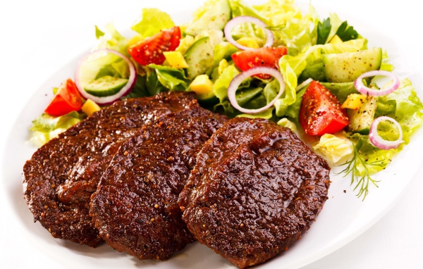Три котлеты на тарелке с салатом на белом фоне