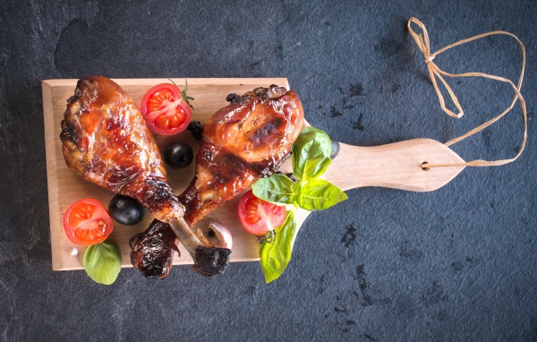 Две зажаренных куриных ножки с овощами на разделочной доске