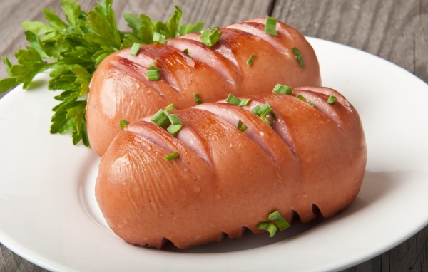 Два жареные сардельки на большой белой тарелке с зеленью 