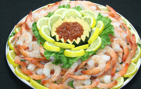 Вареные креветки с лимоном и соусом на большой тарелке