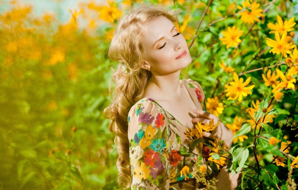 Красивая блондинка нежится в лучах солнца у желтых цветов