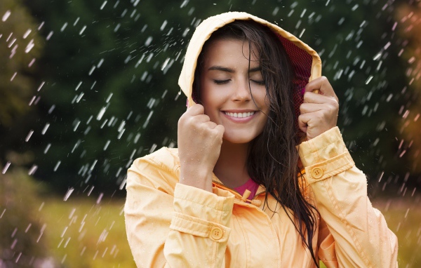 Красивая молодая девушка в желтом плаще стоит под дождем