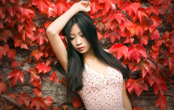 Молодая девушка азиатка стоит у стены с красными листьями