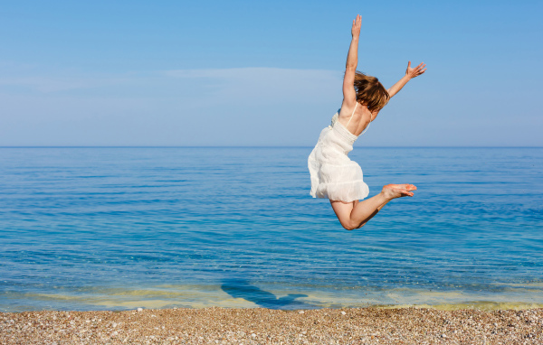 Молодая девушка в белом платье делаем прыжок на песке у моря