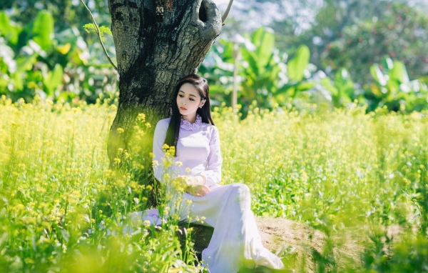 Красивая девушка азиатка сидит в белом платье под деревом