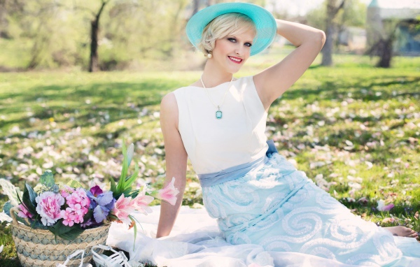 Красивая блондинка в голубой шляпке сидит в парке на траве