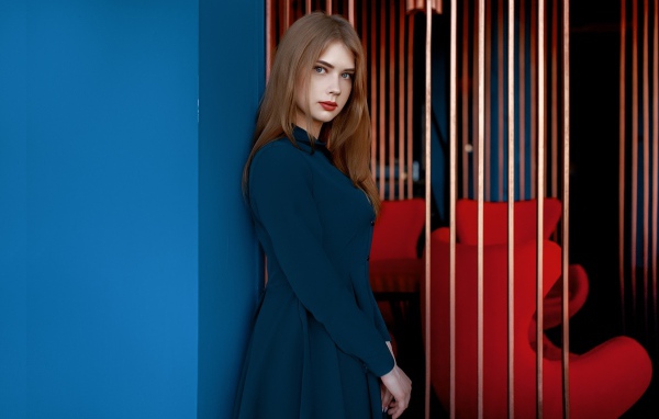 Красивая голубоглазая девушка стоит в пальто у стены