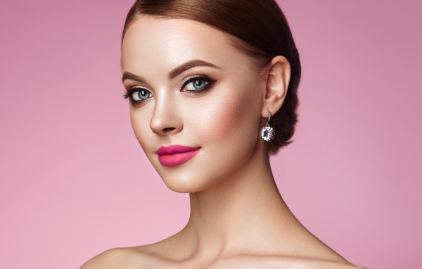 Красивая голубоглазая девушка с красивыми серьгами на розовом фоне
