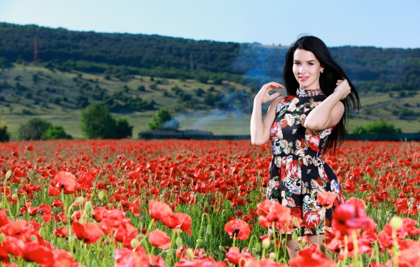 Красивая брюнетка стоит на поле с красными маками