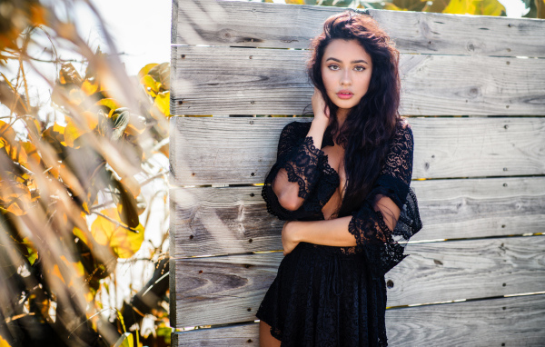 Красивая девушка в черном платье у стены 