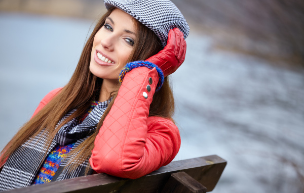 Красивая девушка в красной куртке сидит на лавке