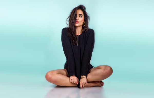 Красивая девушка сидит в черном свитере на голубом фоне
