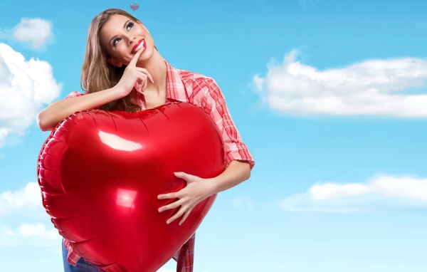 Красивая девушка с большим воздушным шаром в форме сердца на фоне неба