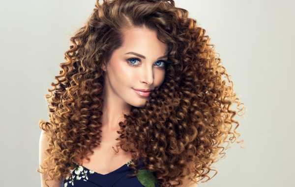 Красивая девушка с длинными волнистыми волосами на сером фоне