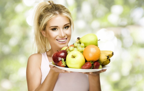 Красивая улыбающаяся блондинка с тарелкой с фруктами в руках