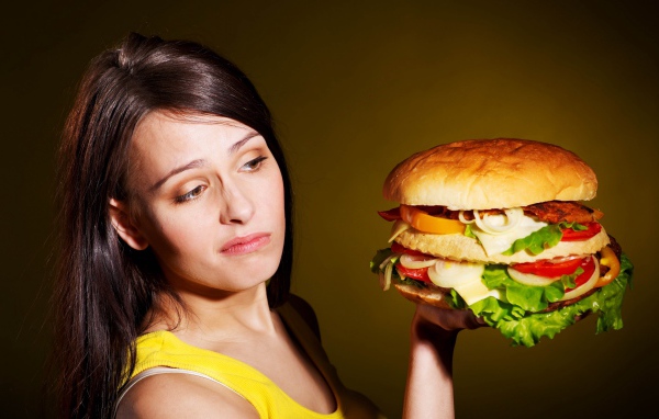 Недовольная девушка с большим гамбургером в руках 